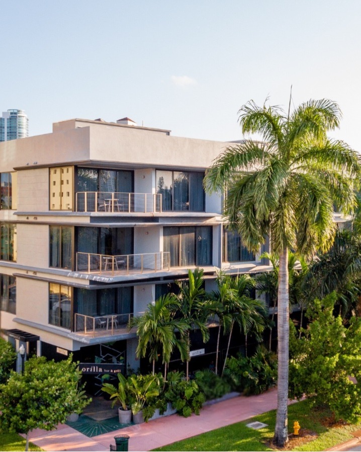 A multi-story building with balconies and palm trees in front.