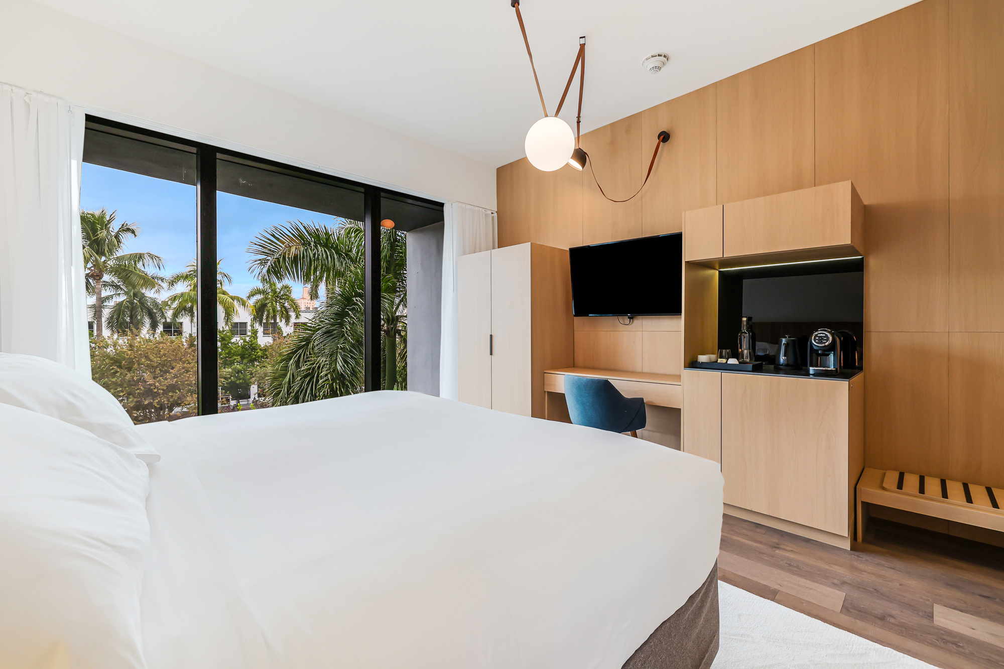 A modern hotel room with a large window, a desk area, and a coffee maker.