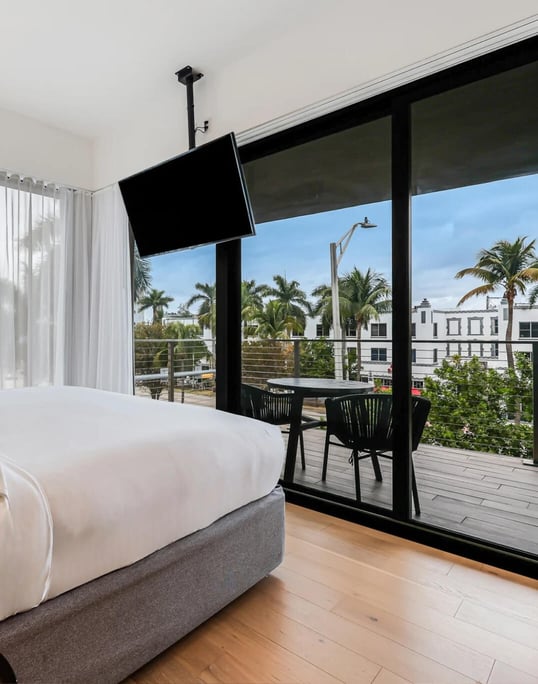 A hotel bedroom with a plush bed and a balcony overlooking tropical palm trees.