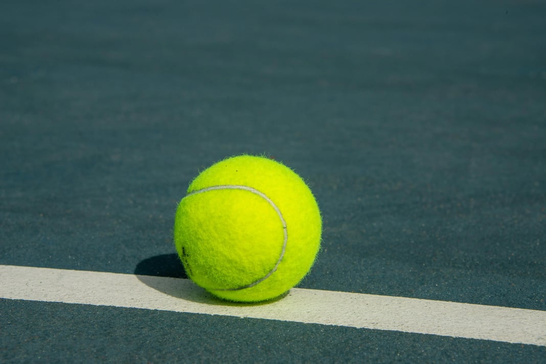 Bright yellow tennis ball resting on the white line of an outdoor tennis court