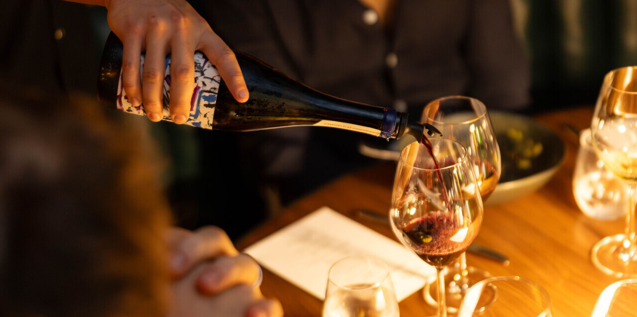 A person pouring wine into a glass on a table set for dining.