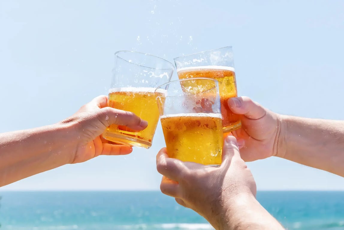 Friends toasting with cold beer by the ocean