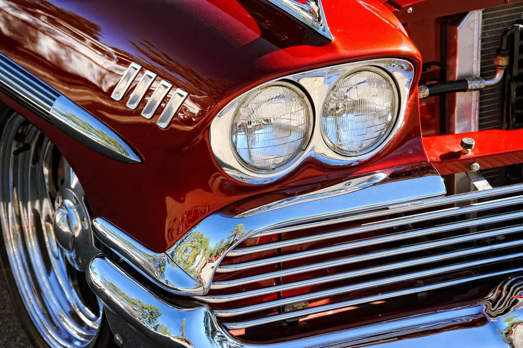 A close-up of the front of a shiny, metallic red classic car.